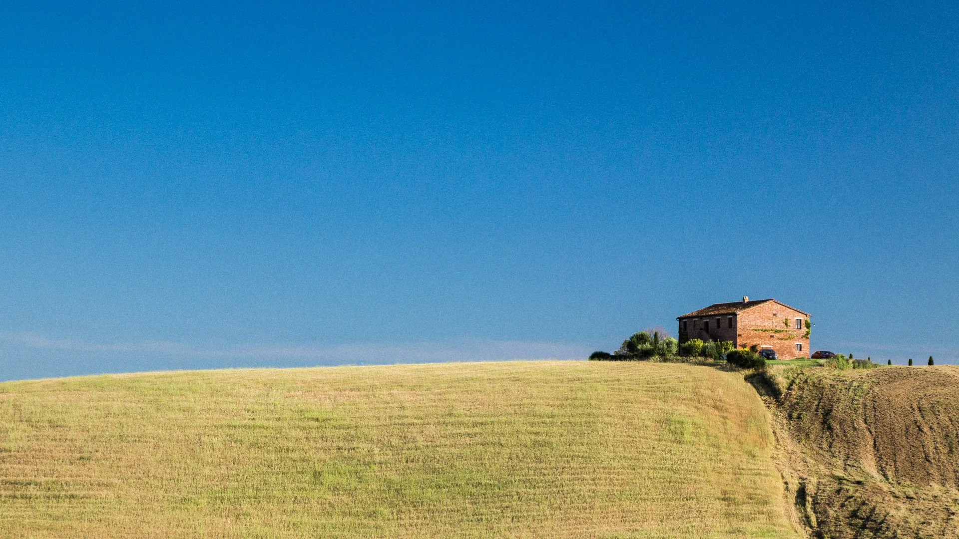 Brick farmhouse on a golden ridge under a deep blue sky