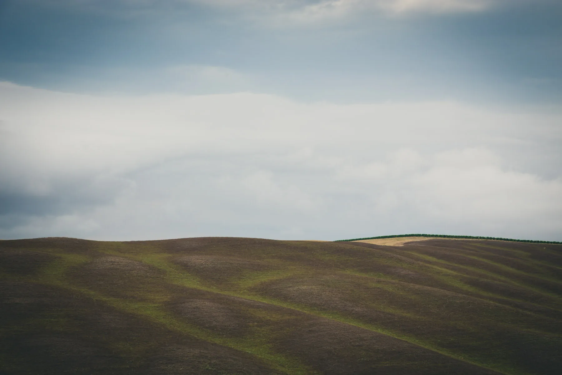 Dark rolling hill beneath a band of pale light and grey cloud