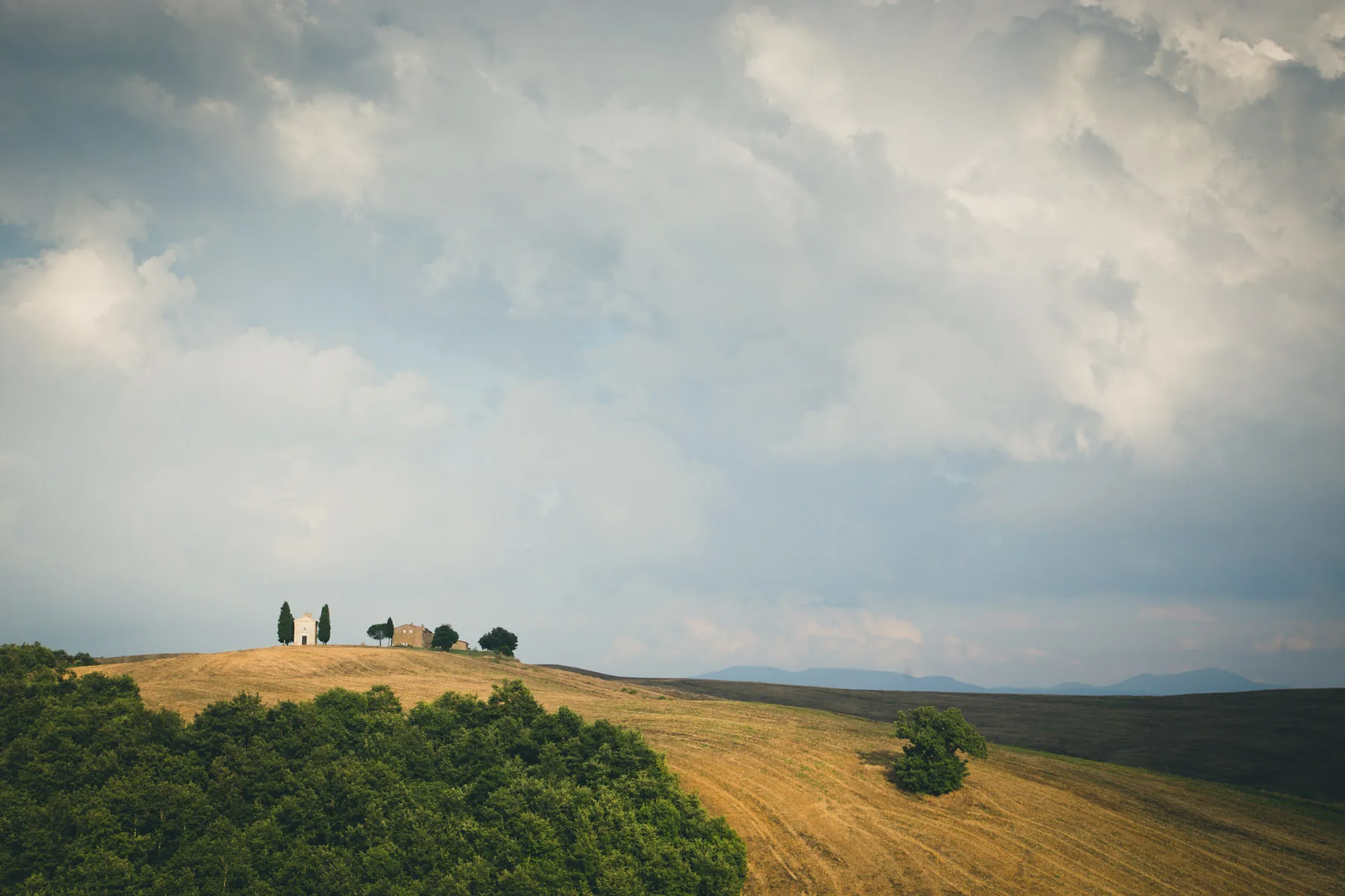 Distant chapel on a hilltop above woods under a pale cloudy sky