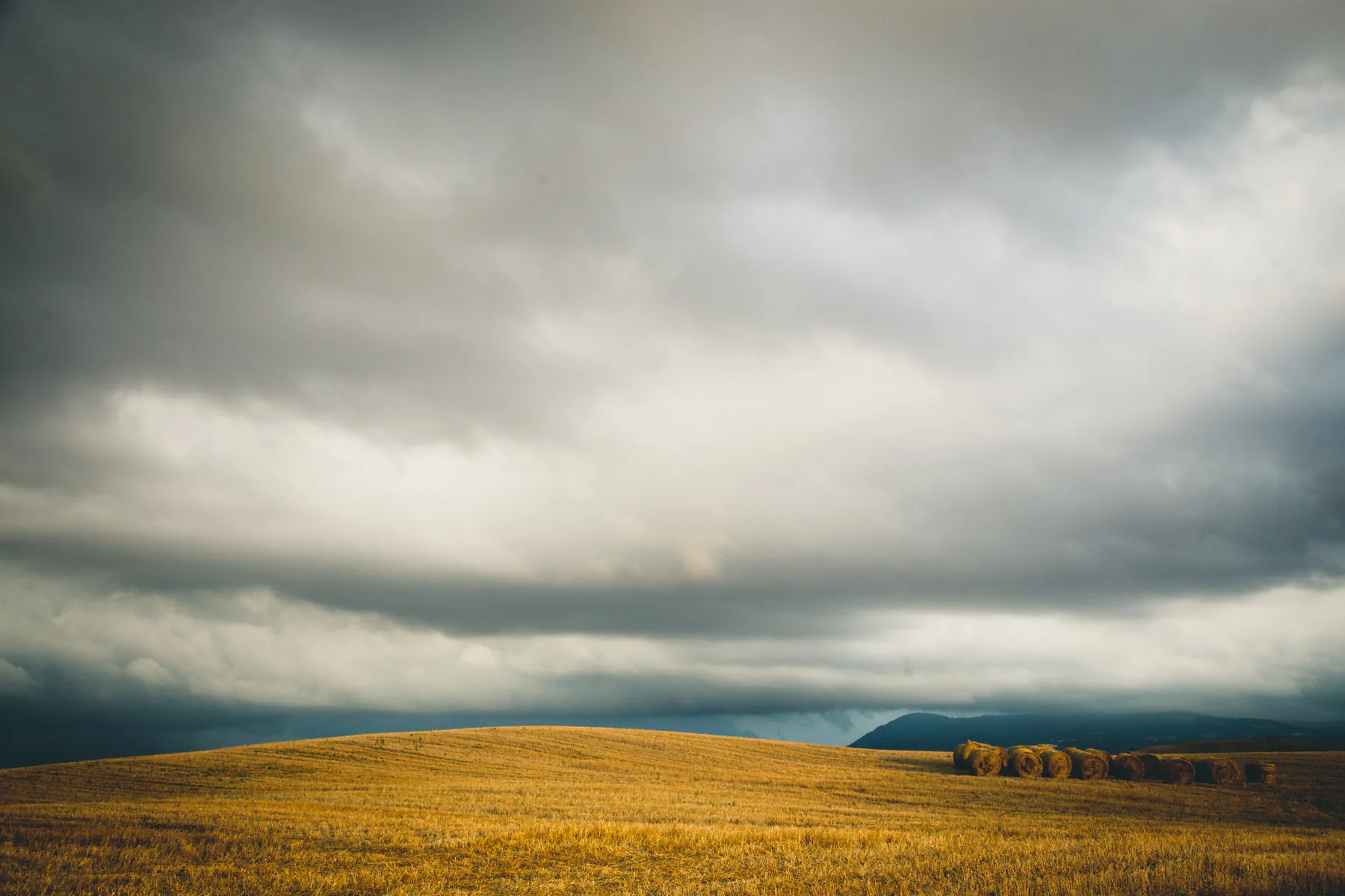 Storm clouds massing over a harvested golden hillside