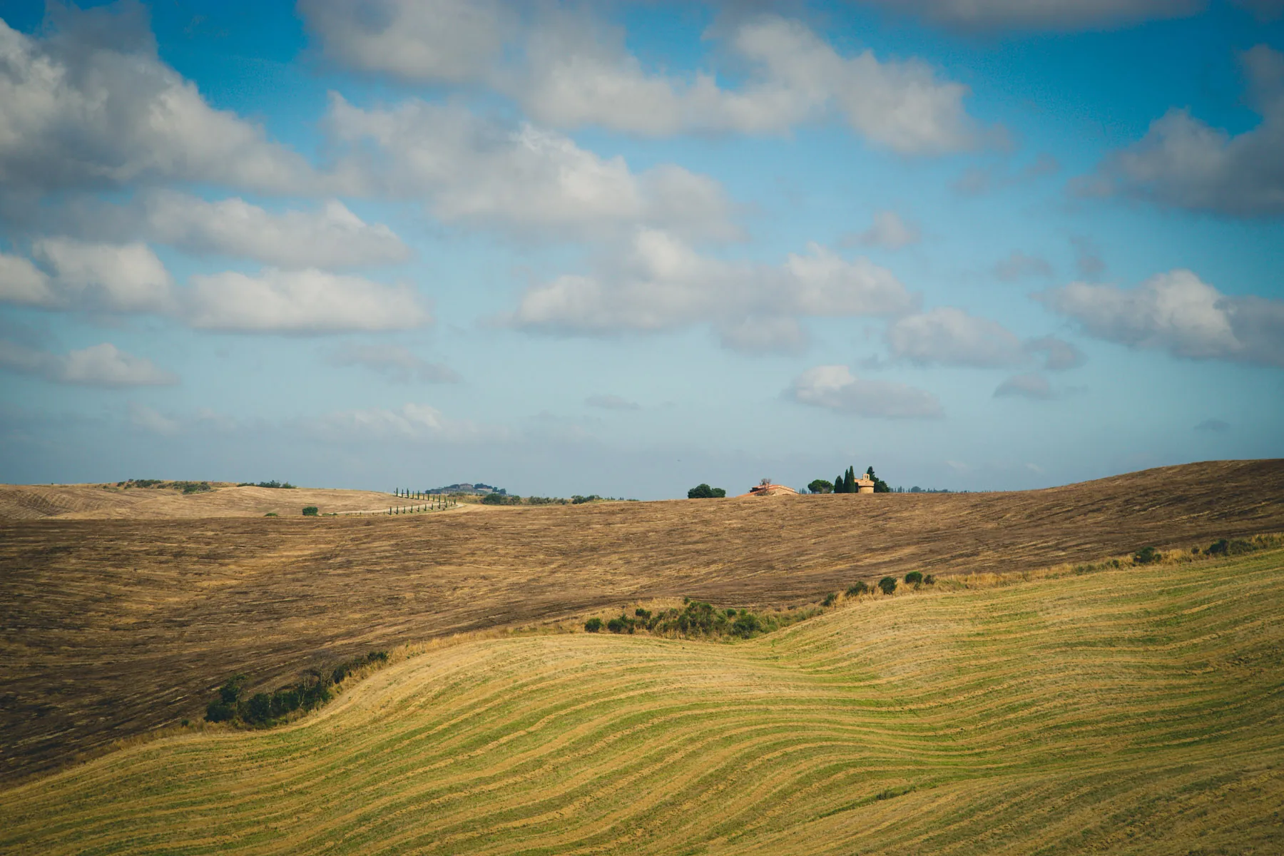 Ochre hills with a distant farmhouse beneath a cloud-filled sky