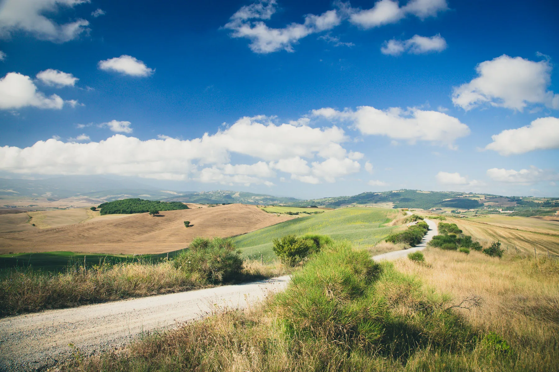 White gravel road winding through fields under scattered clouds