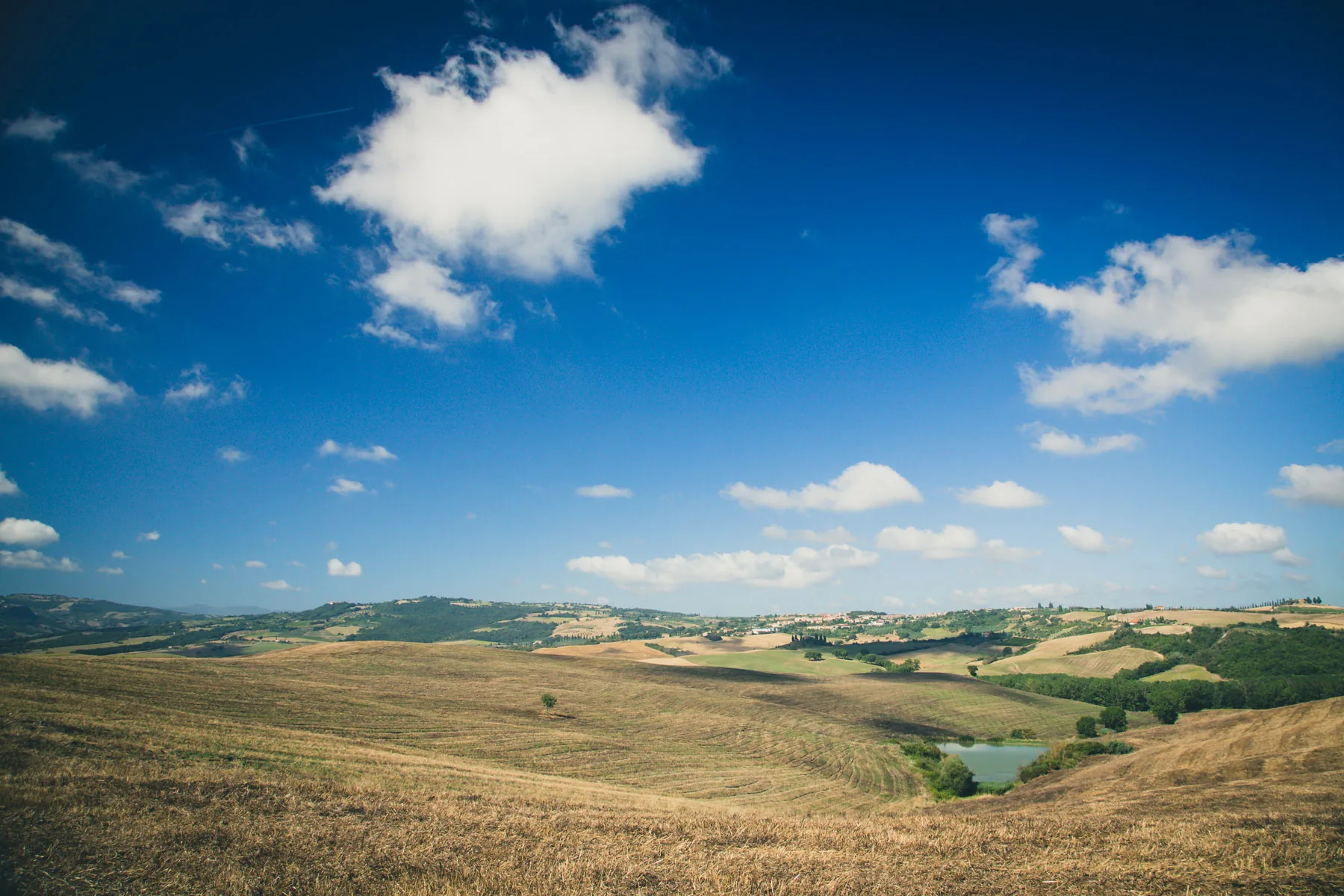 Wide valley with a small pond beneath a deep blue sky and clouds