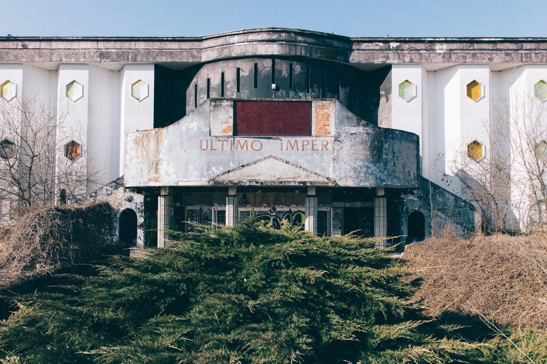The rounded facade of an abandoned disco club behind overgrown shrubs