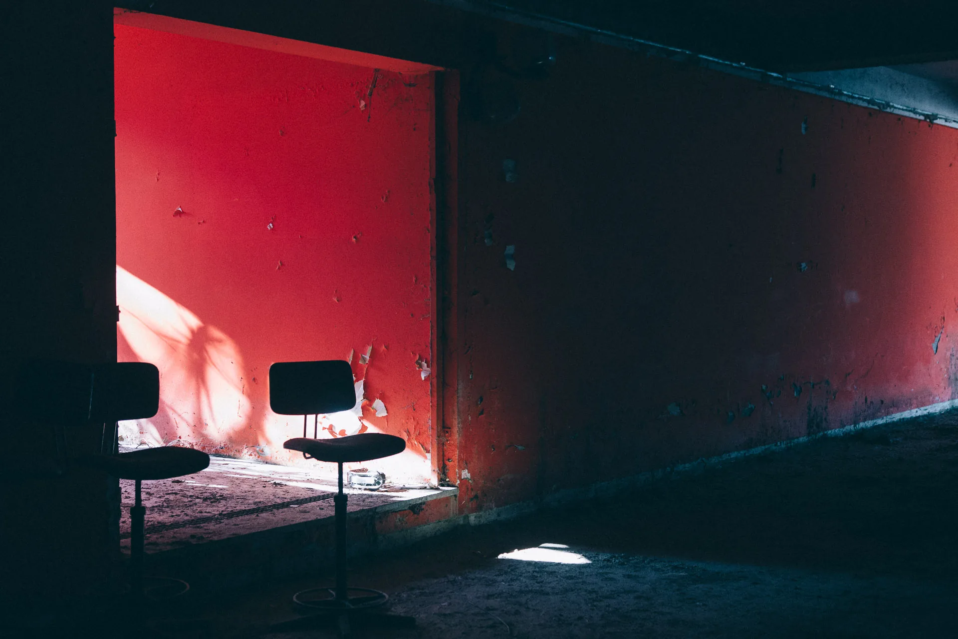 Two chairs in a shaft of light against a red wall