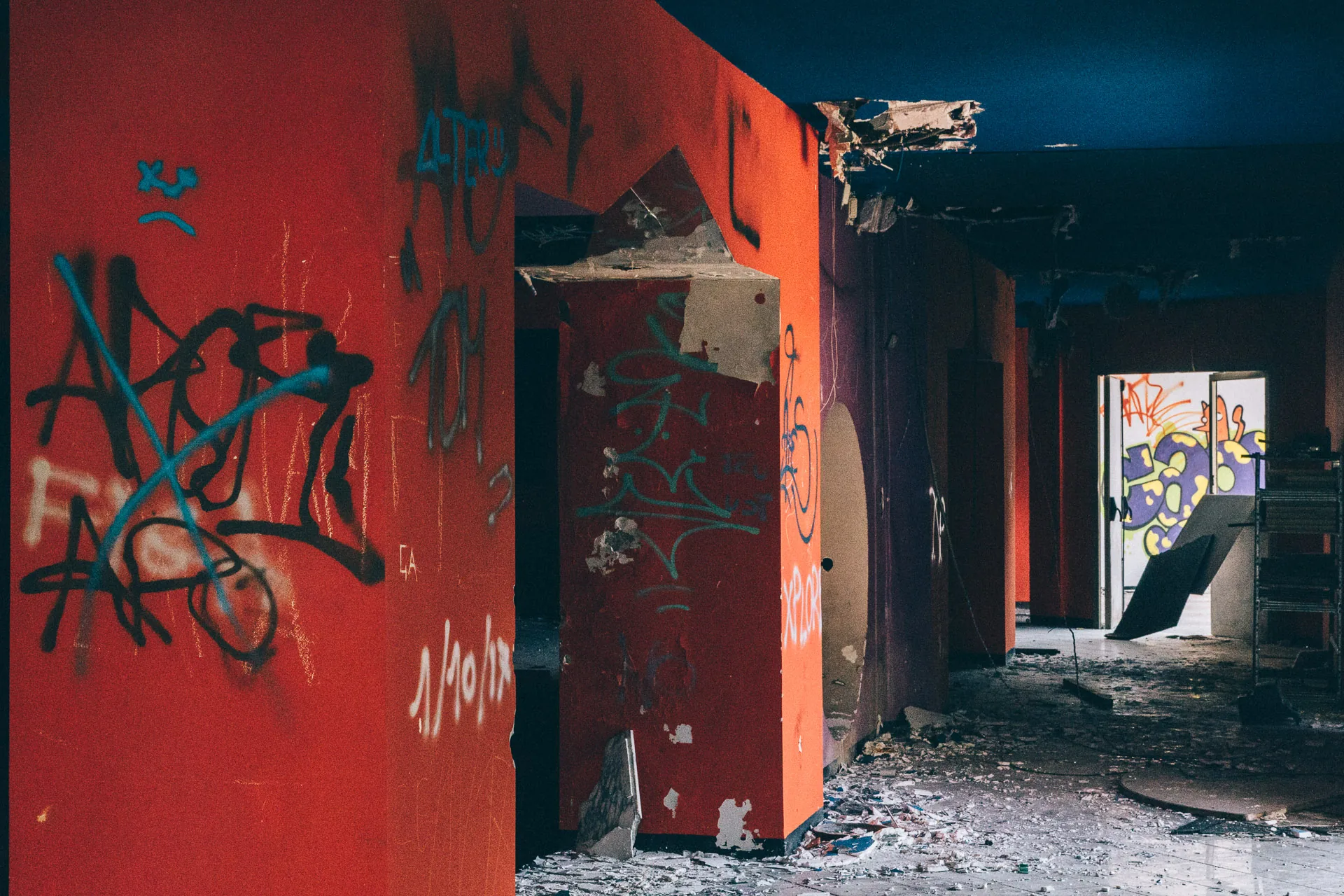 Graffiti-tagged red walls opening onto a derelict corridor