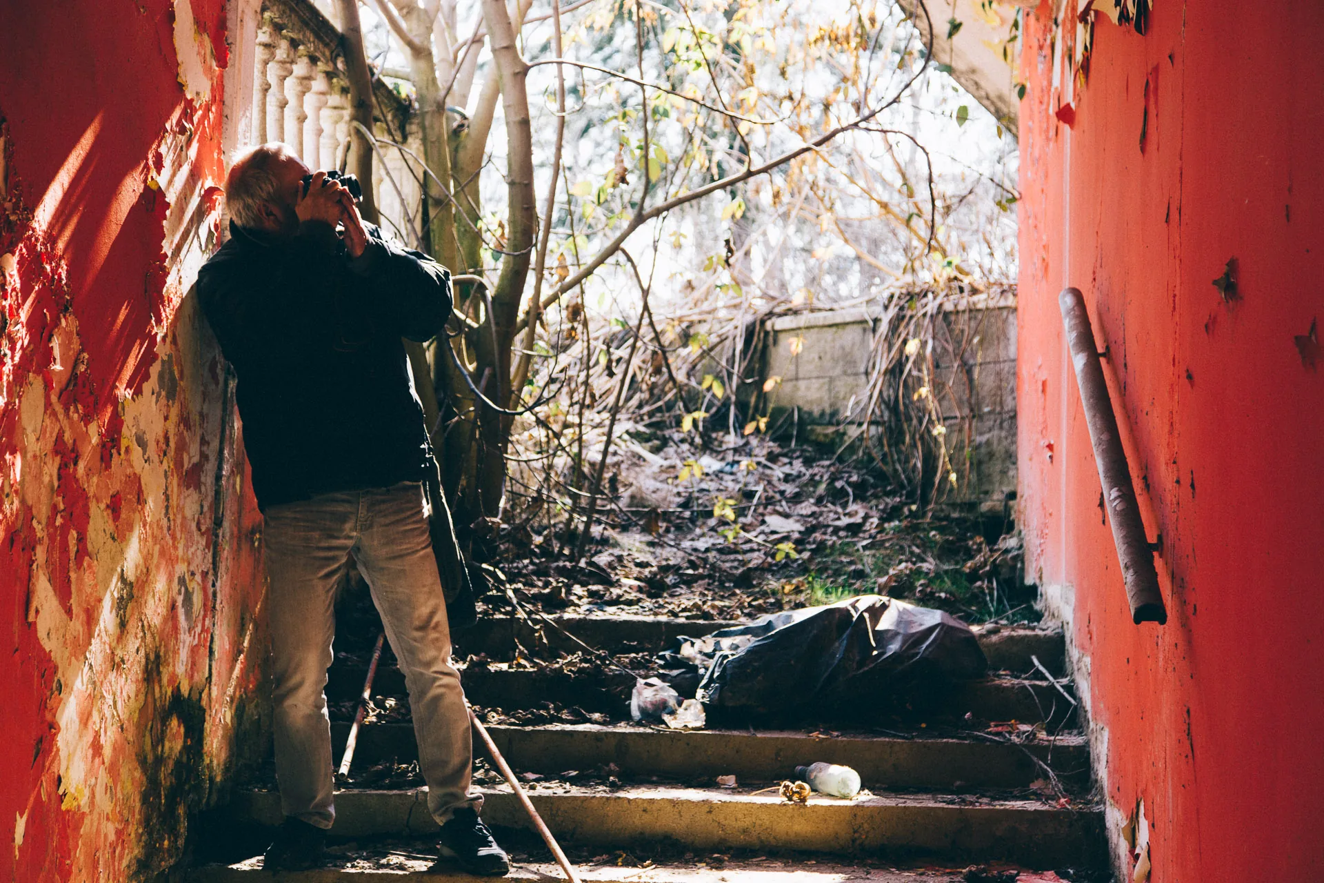 A friend climbing overgrown steps beside a red wall