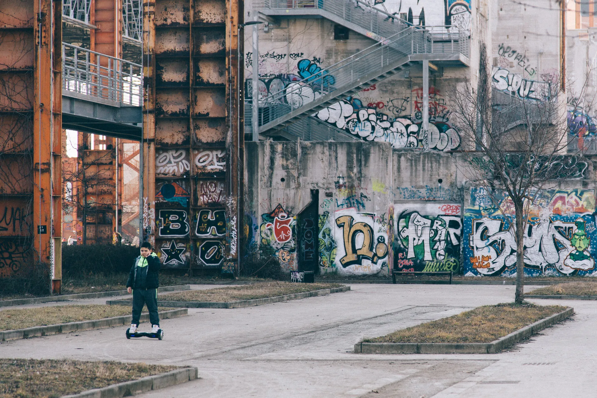 A graffiti-covered wall under brick factory buildings