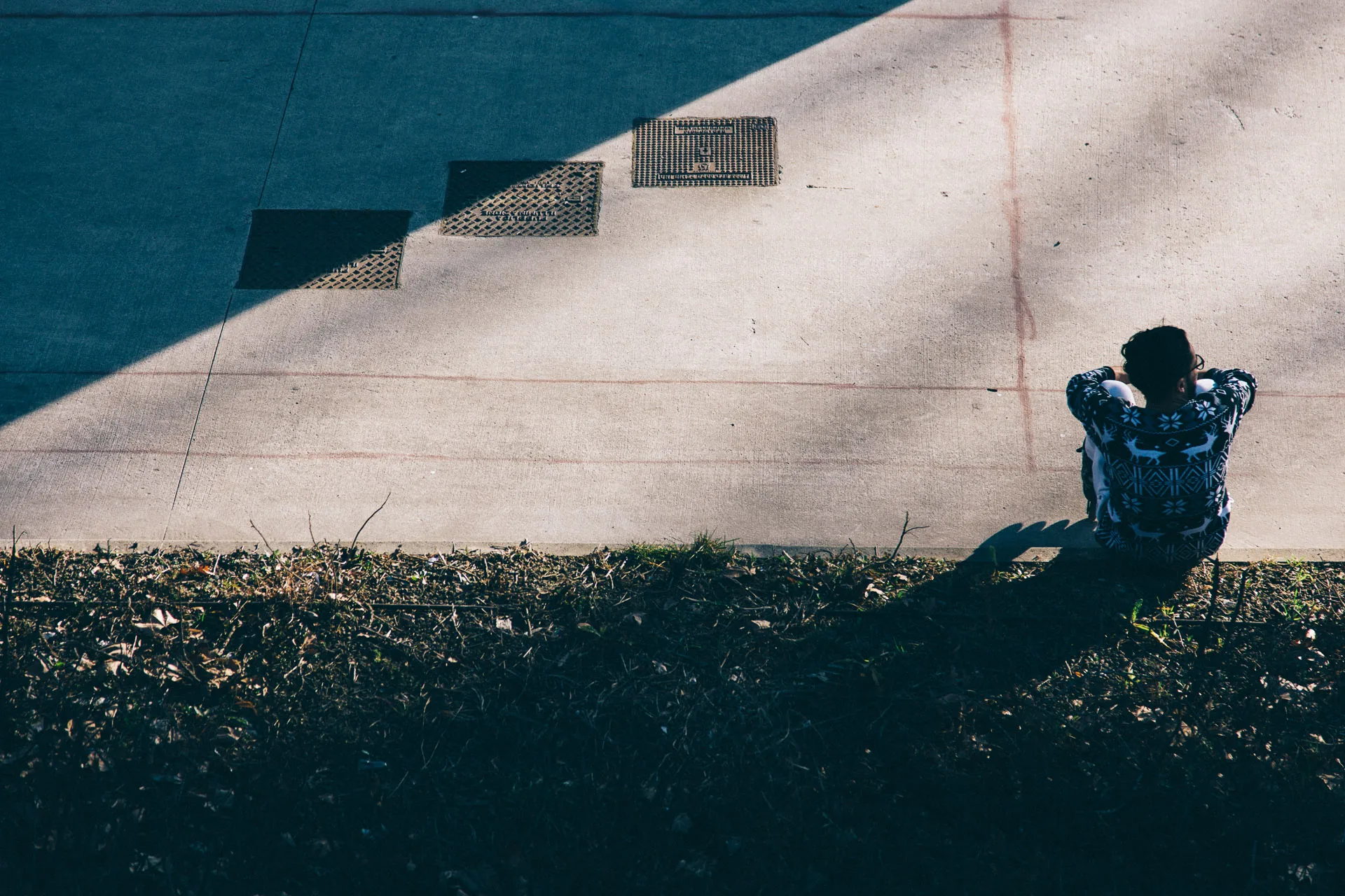 A man sitting on a grassy slope against a sunlit wall